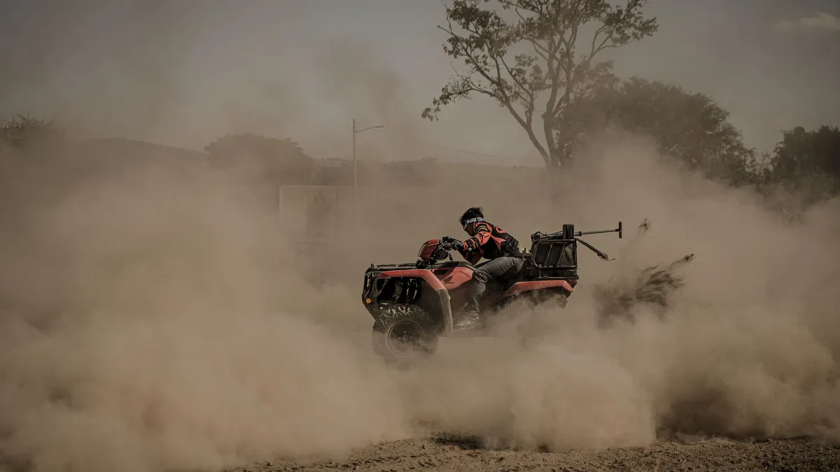 Man riding a quad bike through dusty off-road terrain, showcasing adventure and thrill.