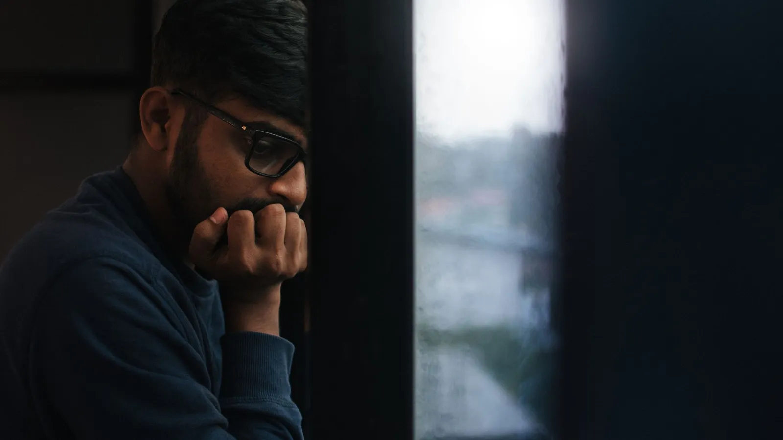 Contemplative man gazing out a rainy window, lost in thought.