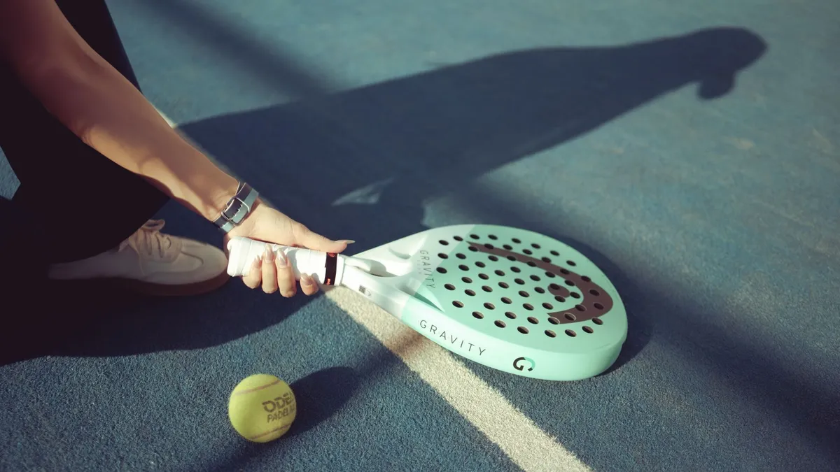 Padel player holding a racket on a sunlit court in Baghdad, Iraq.