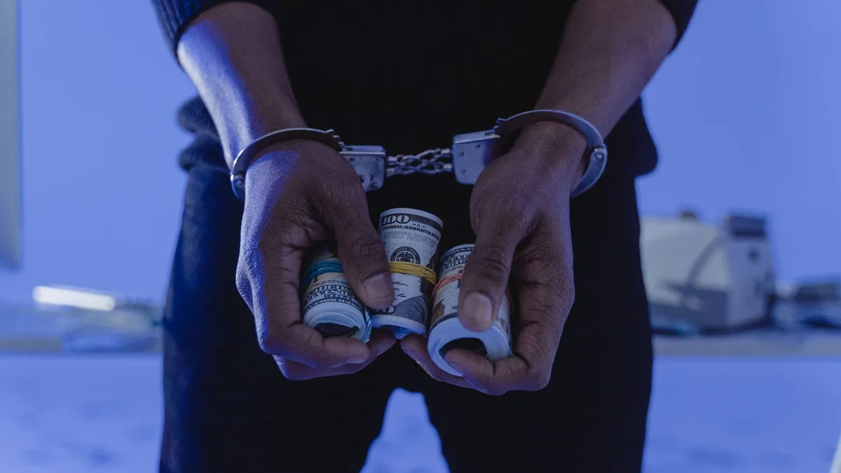 Close-up of handcuffed hands holding rolled cash, suggesting crime or arrest.