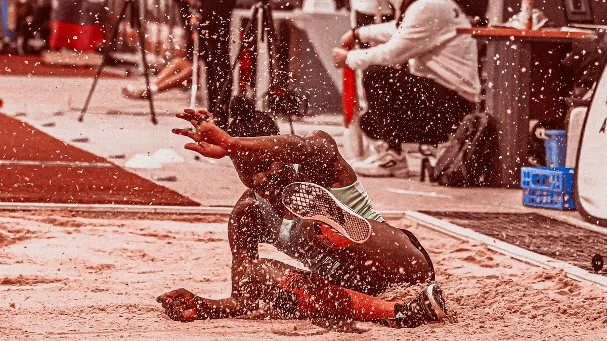 Athlete landing in sand during a long jump competition, showcasing athleticism and motion.