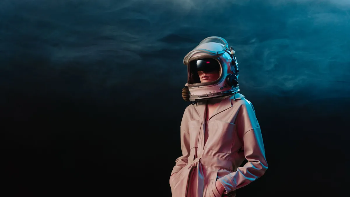 Stylish woman in astronaut suit standing in a dramatic studio setting with moody lighting.