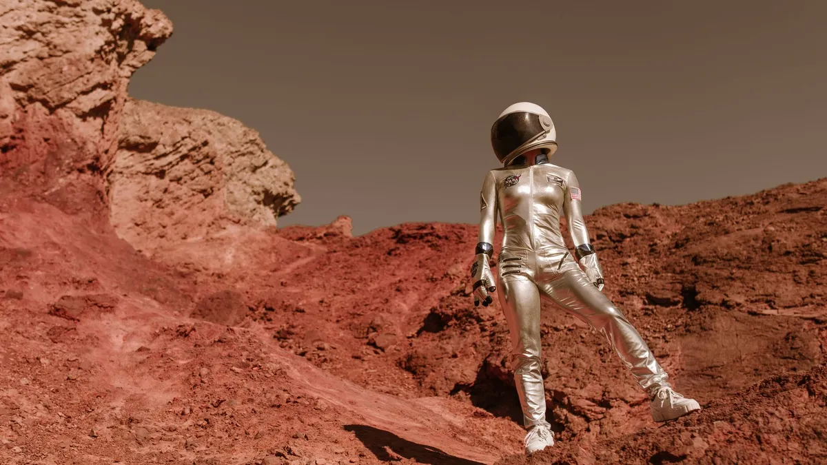 Astronaut in space suit standing on red rocky terrain resembling Mars' surface.