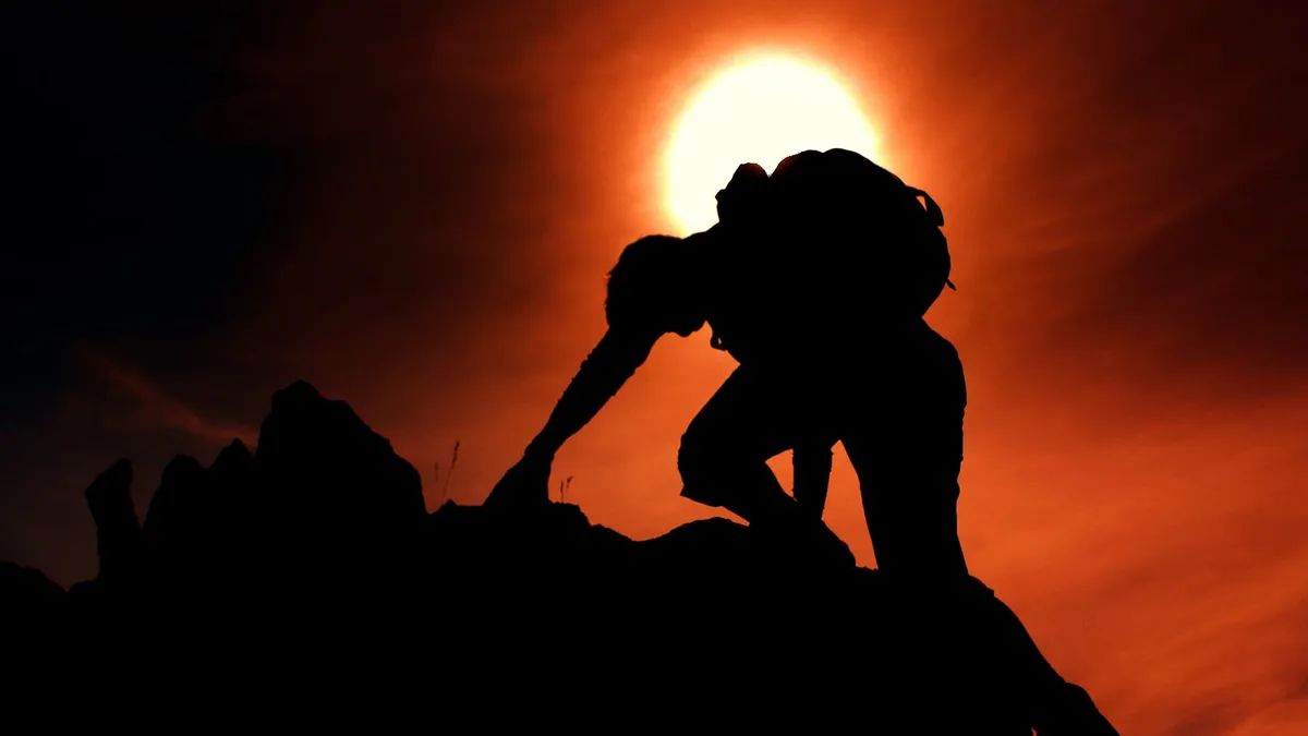 Dramatic silhouette of a climber scaling rocks against a vibrant sunset in Nordland, Norway.