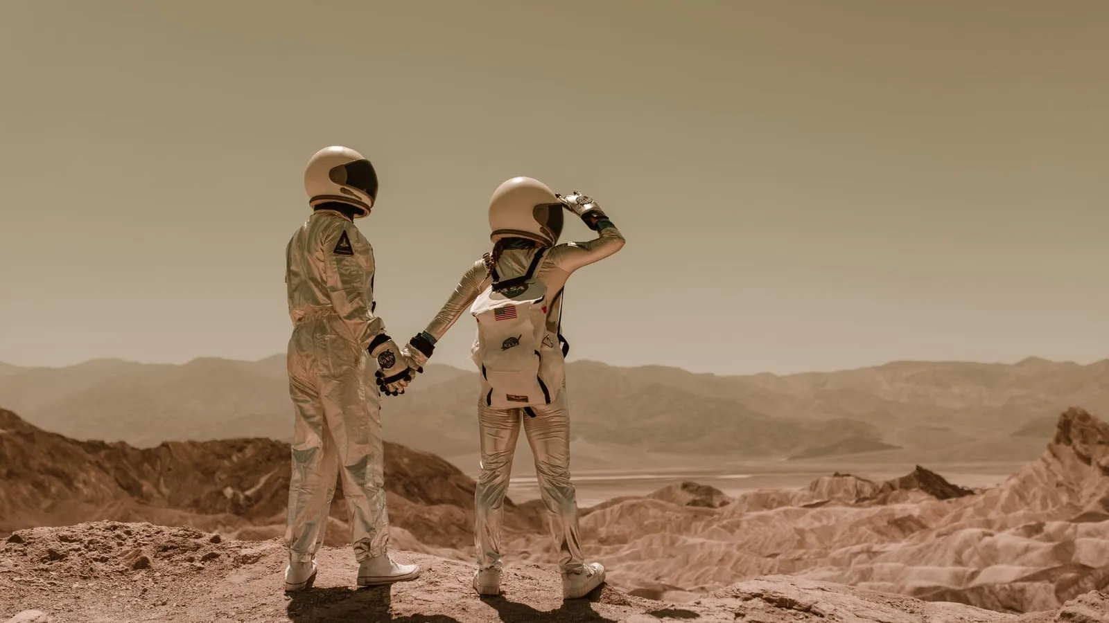 Two astronauts holding hands, exploring rocky Mars-like terrain. — Photo by RDNE Stock project on Pexels