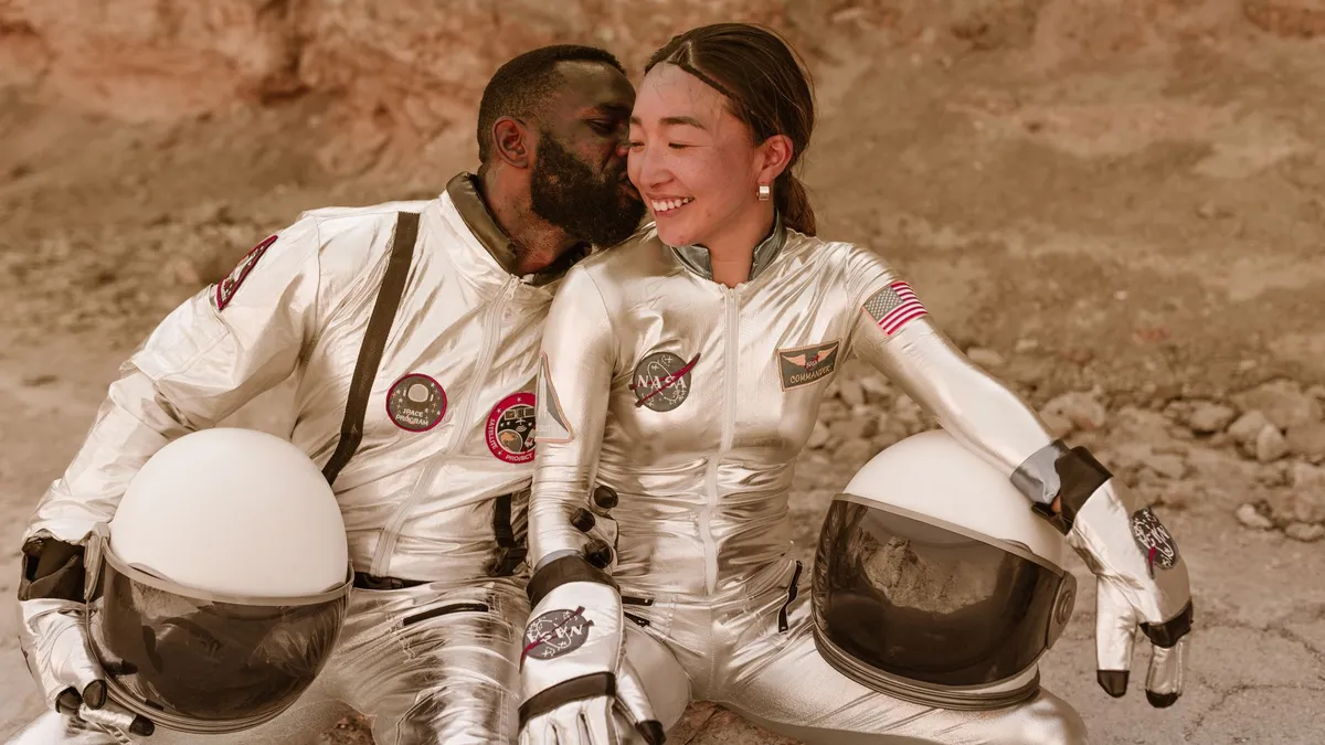Interracial couple in silver astronaut costumes sharing a kiss on a rocky terrain, evoking space exploration romance. — Photo by RDNE Stock project on Pexels