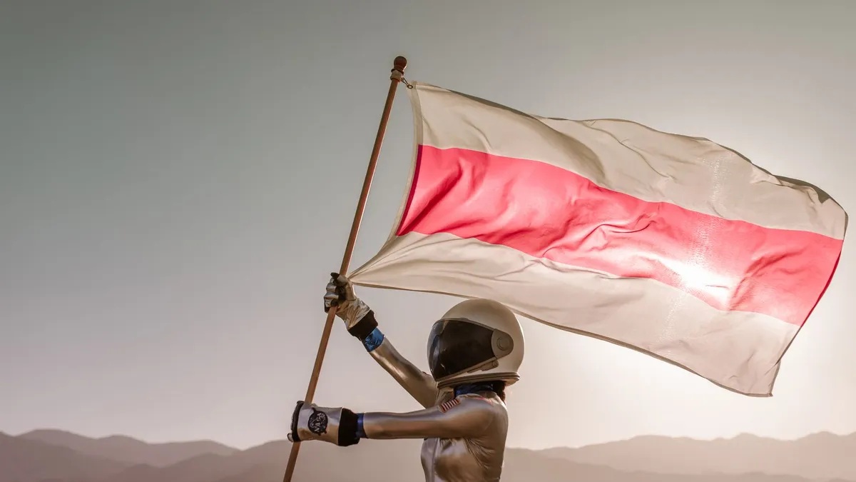 Astronaut in space suit holding a red and white flag in a barren desert setting, against a bright sky. — Photo by RDNE Stock project on Pexels