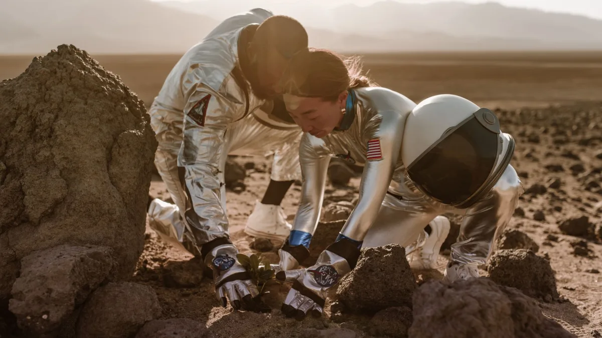 Two astronauts planting a seedling in a rocky desert terrain, symbolizing space colonization. — Photo by RDNE Stock project on Pexels