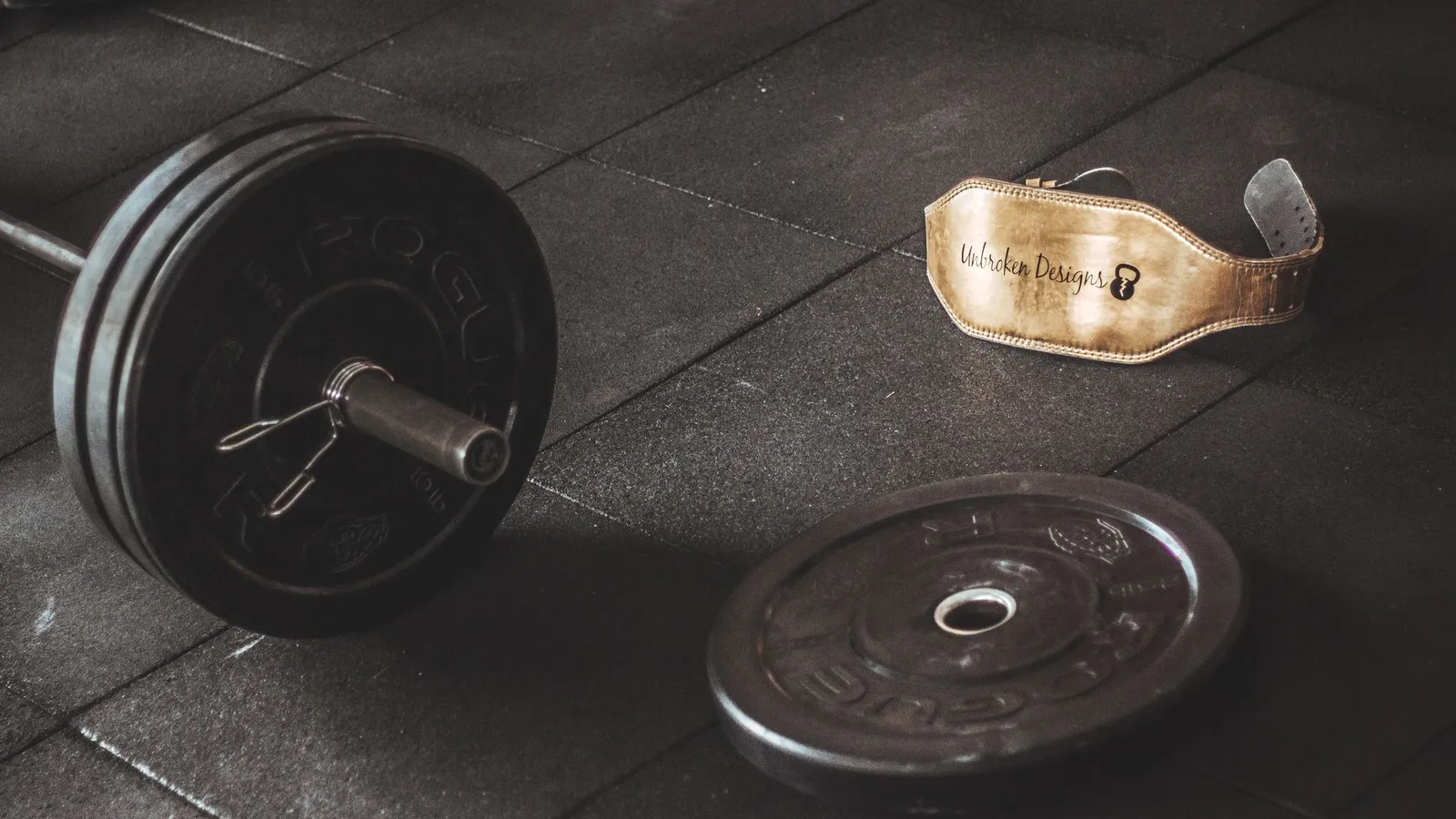 A heavy barbell and weightlifting belt on a gym floor, emphasizing strength and fitness. — Photo by Victor Freitas on Pexels